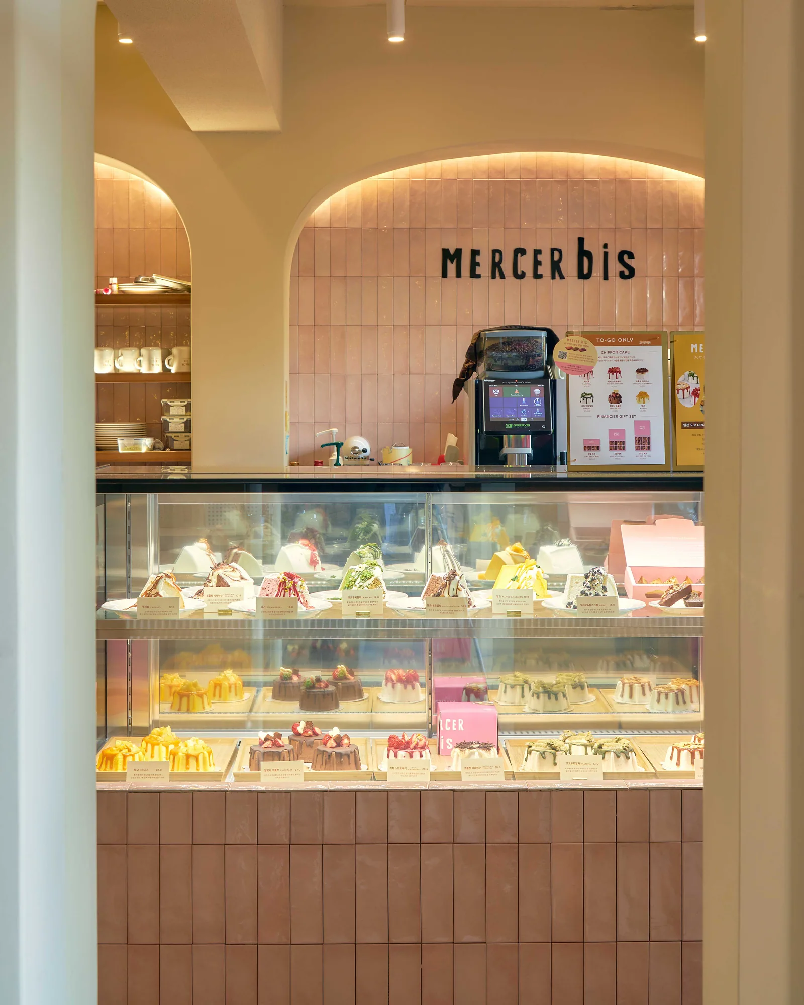 블러시 핑크 타일 아치와 벽면 MERCERbis 사인, 쉬폰케이크가 진열된 쇼케이스